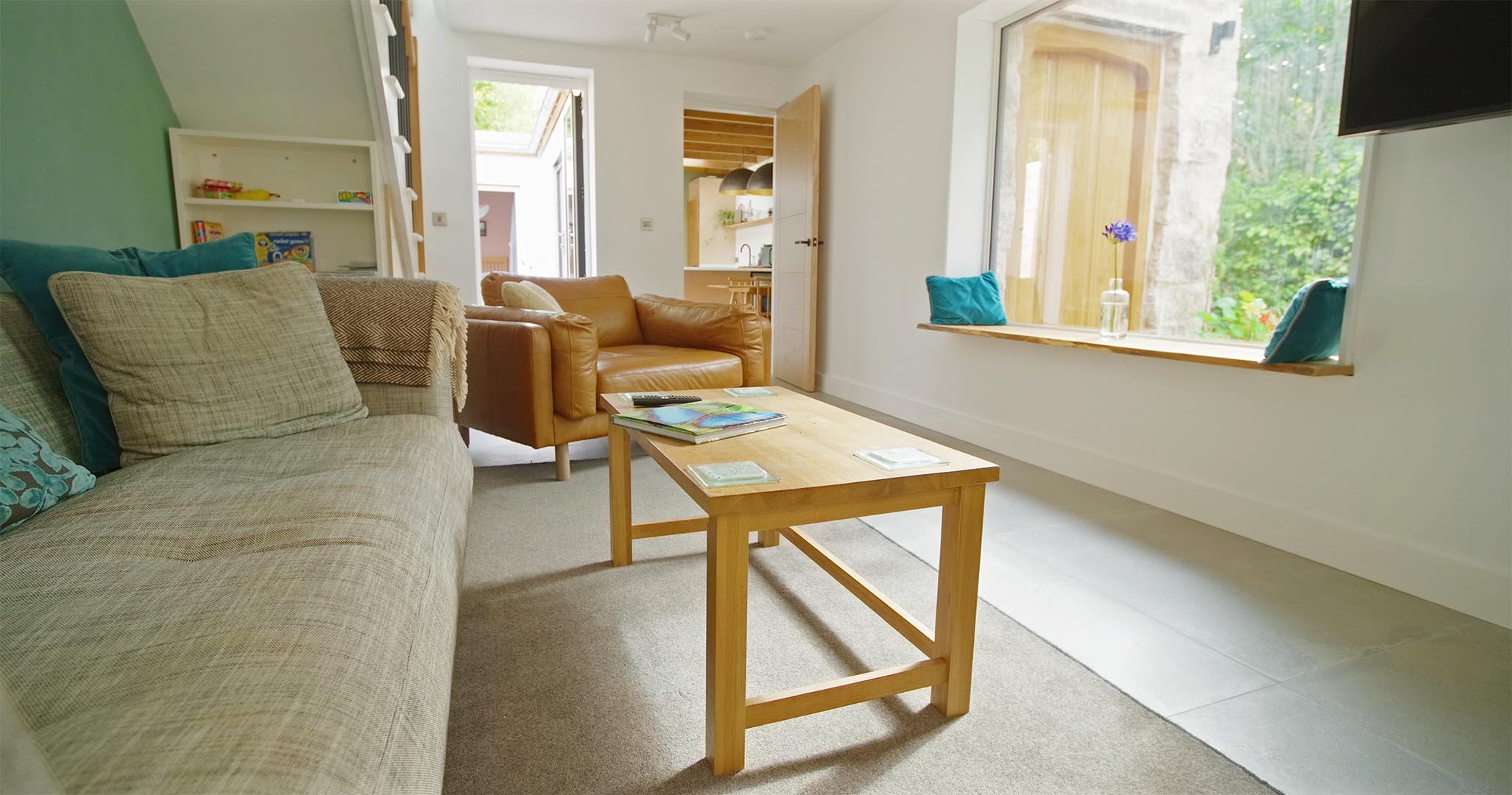 Wide angle view of the lounge at Fernleigh Courtyard holiday cottage, with sofa, leather loveseat & oak coffee table.