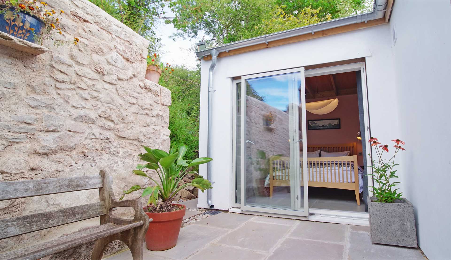 Paved courtyard with stone wall and open sliding door to ground floor bedroom at Fernleigh Courtyard holiday cottage.