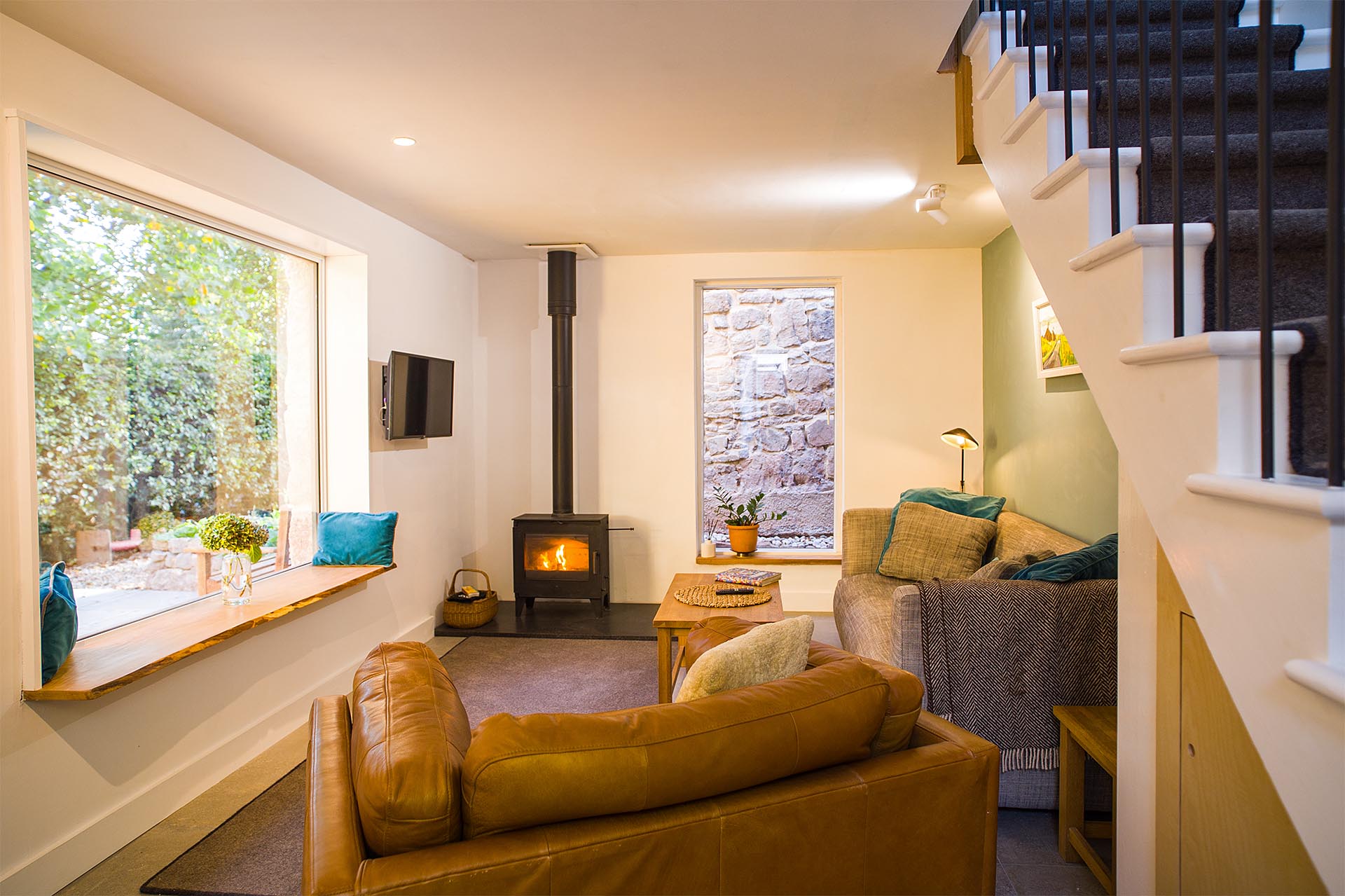 Internal view of the lounge at Fernleigh Courtyard showing a loveseat, large sofa, lit woodburner, and picture windows.