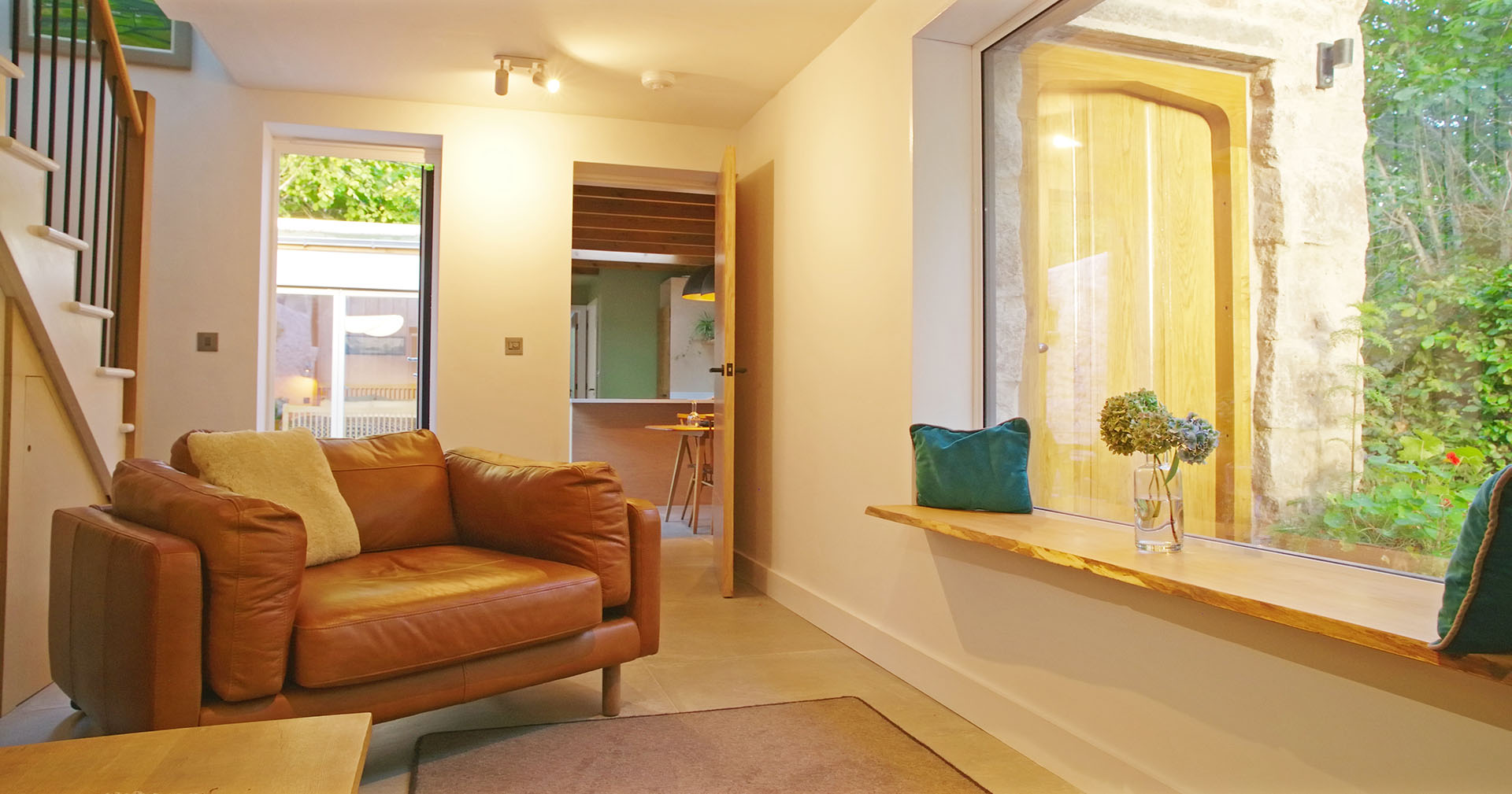 Internal view of the lounge at Fernleigh Courtyard showing doorway to the kitchen-diner beyond leather loveseat, with picture window..