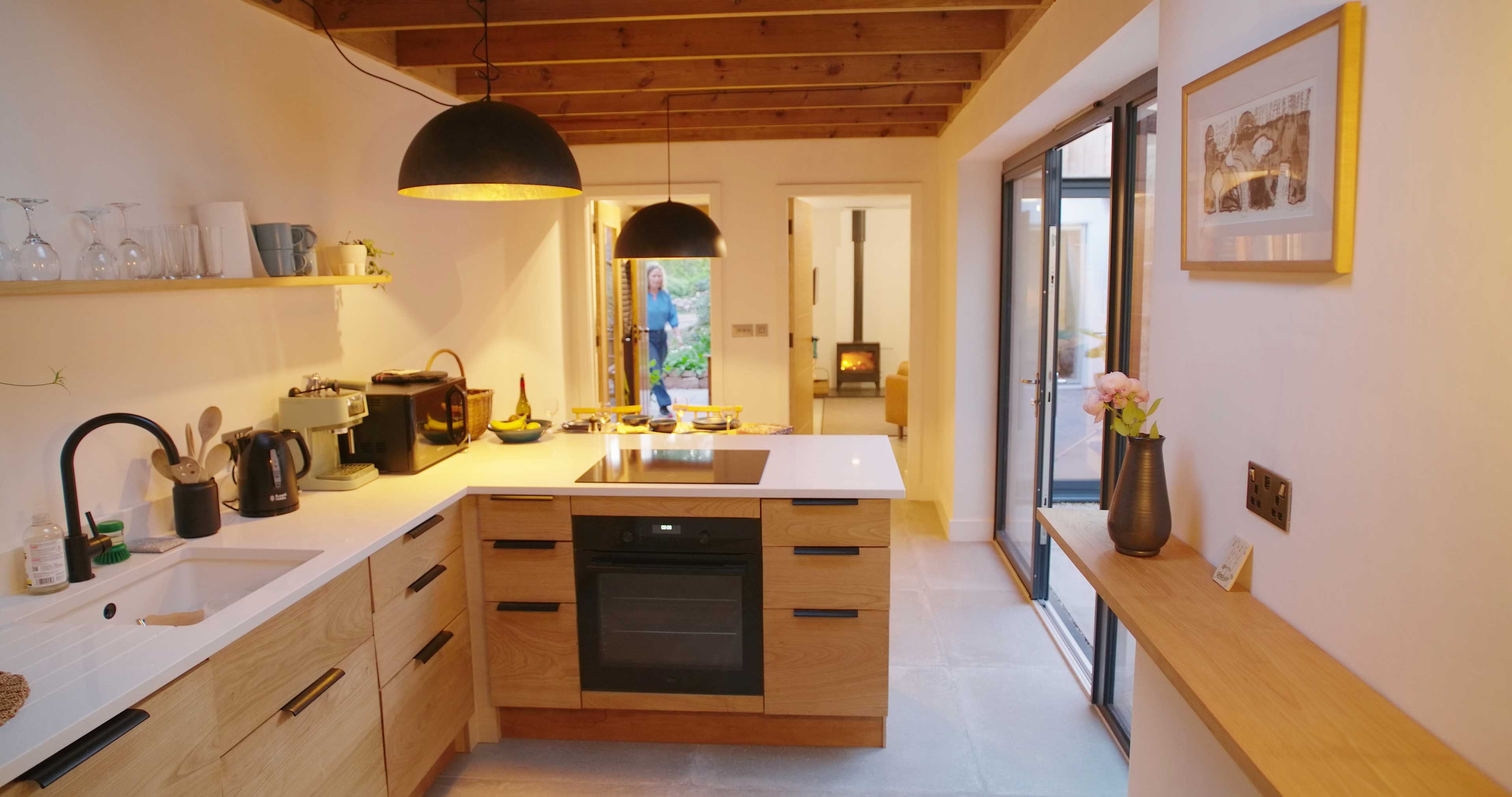 Bespoke kitchen long view with open front door and woodburner fire in the lounge at Fernleigh Courtyard holiday cottage.