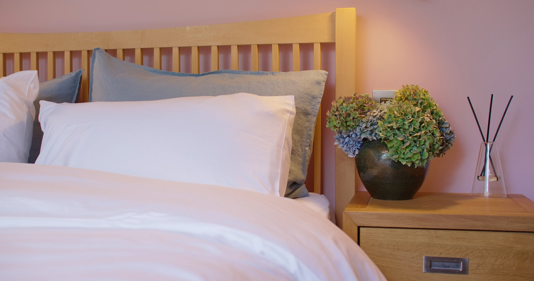 Bedside flowers, cotton and linen pillows & duvet on the king size wooden bed at Fernleigh Courtyard holiday cottage.