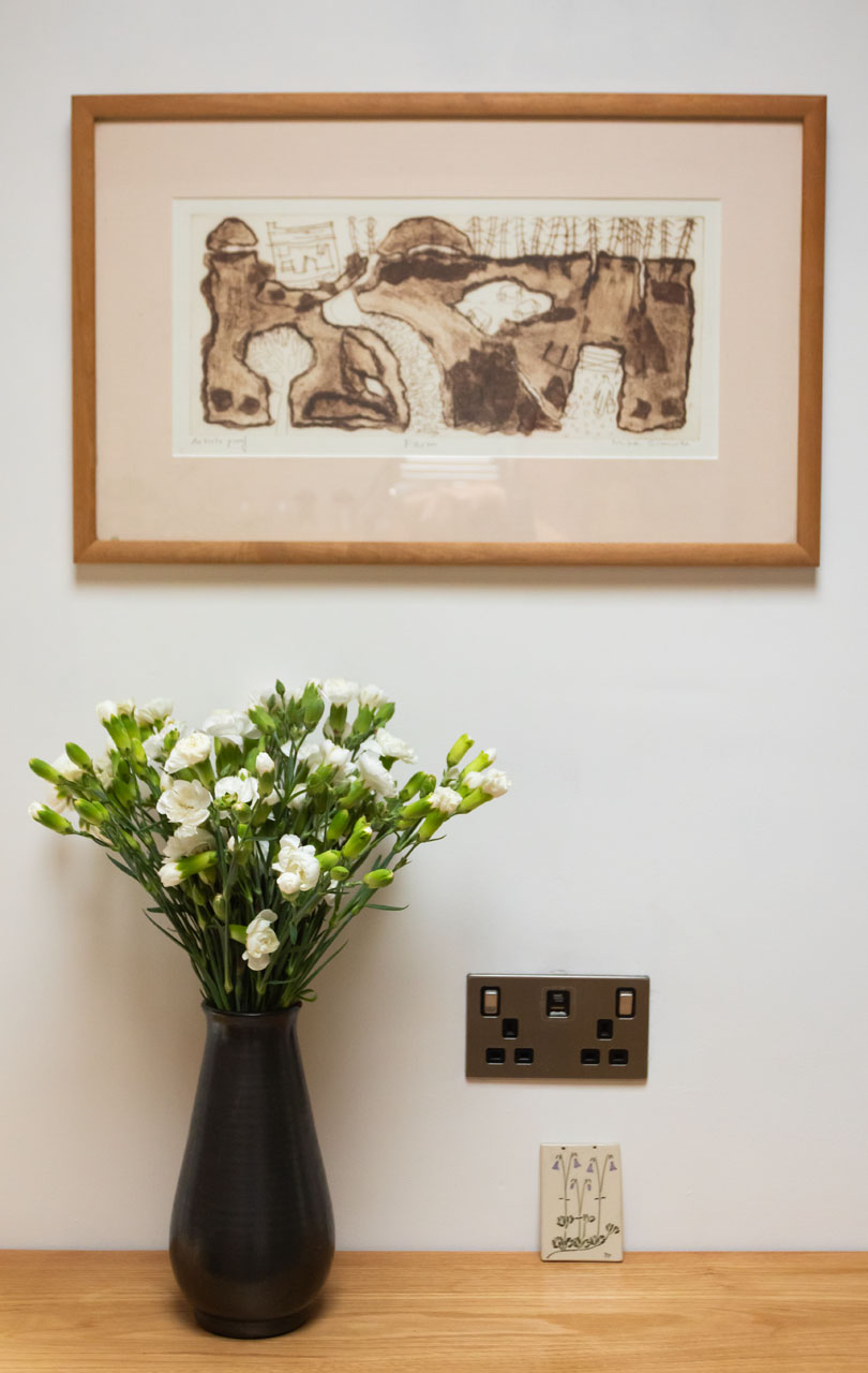 Detail of a shelf with vase holding a bunch of chrysanthemums and picture above at Fernleigh Courtyard holiday cottage.