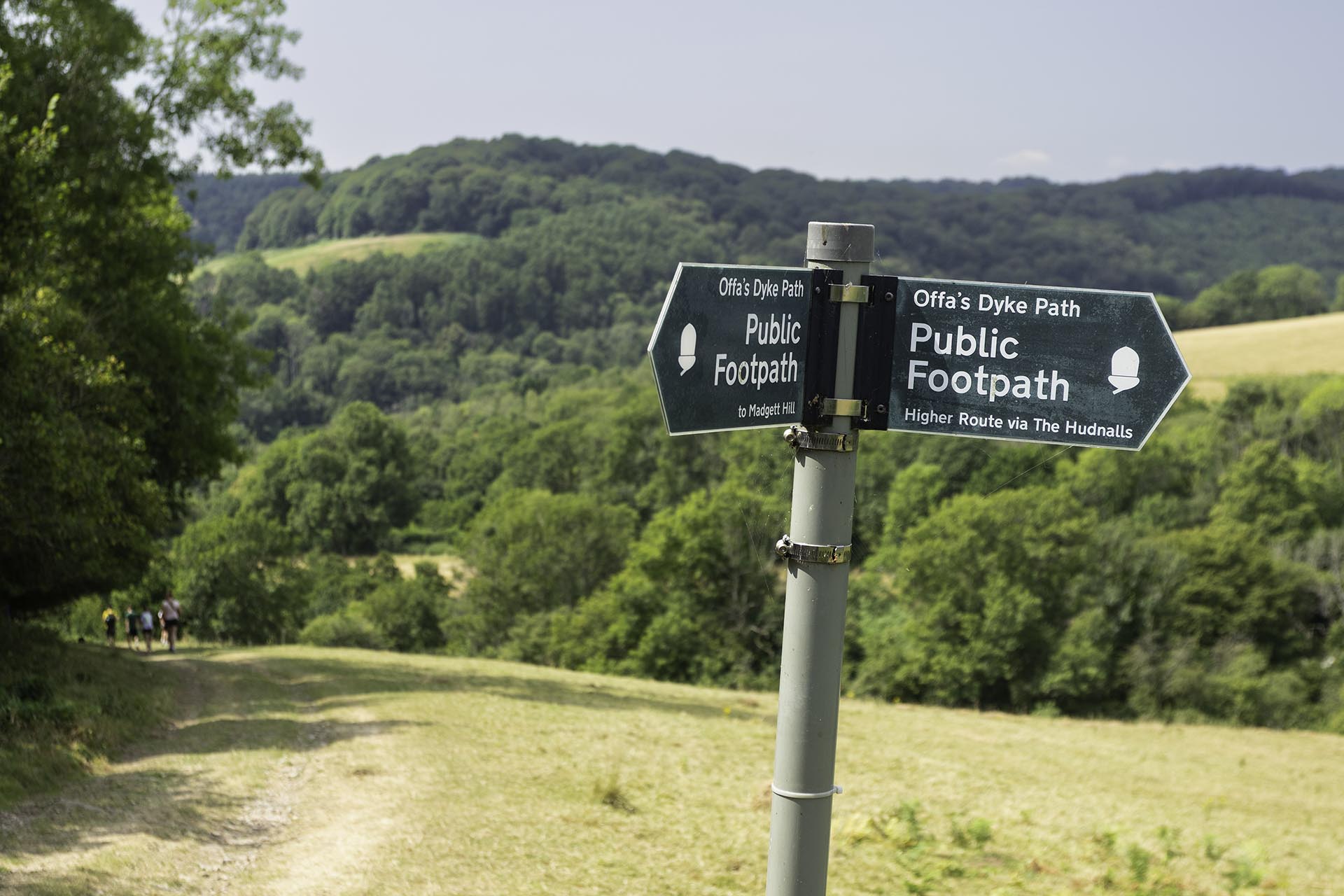 Offa's Dyke signpost and distant walkers in the lower Wye Valley with fields and woodland in the background.